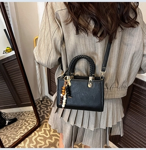 Detail of vintage black crossbody bag featuring woven handles and wooden bead tassel charms