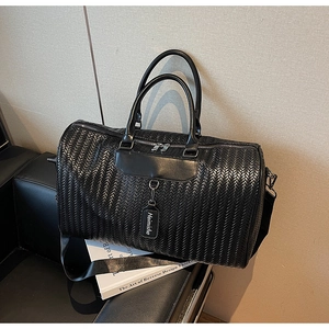 Detail of black woven texture on large travel bag with handles and strap on sofa