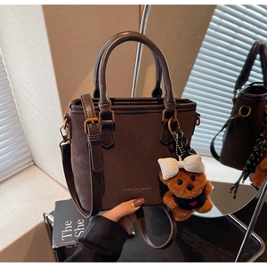 Detail of dark brown leather bucket bag with fashion lettering and cute bear charm