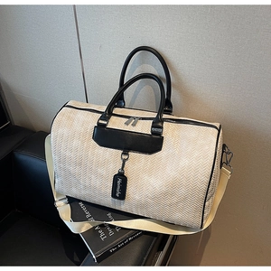 Detail of beige woven travel bag with black leather trim and wide adjustable strap