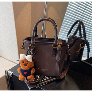 Detail of dark brown tote bag with metal hardware and a cute plush bear charm