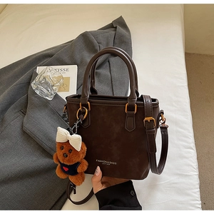 Detailed shot of dark brown leather bucket bag with gold hardware and plush bear charm