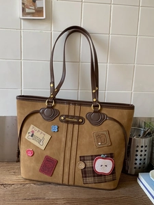 Brown faux suede tote bag with retro patches and long shoulder straps on a desk