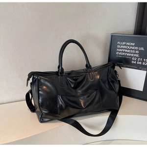 Détail d'un grand sac de voyage en cuir noir avec poignées renforcées et bandoulière large