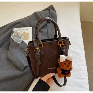 Detailed view of coffee brown tote bag with gold hardware and plush bear charm
