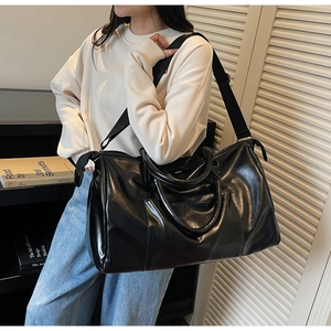 Détail du sac de voyage noir brillant avec poignées renforcées et bandoulière en nylon