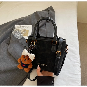 Close-up of black matte leather tote bag with gold lettering and cute brown bear charm