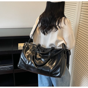 Détail du sac de voyage en similicuir brillant noir avec grande poche et bandoulière