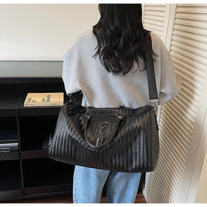 Black woven leather travel bag with adjustable shoulder strap shown on model in indoor setting