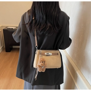 Detail view of khaki matte leather crossbody bag featuring brown strap and bear charm