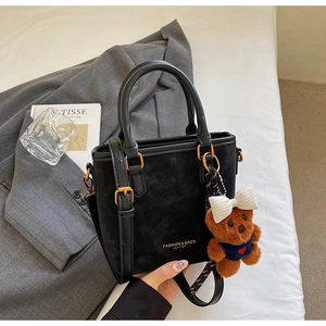 Detail of black suede bucket bag with gold hardware and a cute plush bear charm