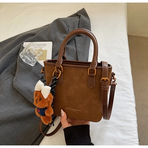 Close-up of brown bucket bag with plush bear charm on minimalist fabric background