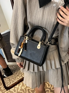 Retro black crossbody bag with woven handle and wooden bead charm worn by a model
