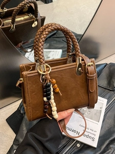 Retro brown PU leather handbag with woven handle and beaded tassel in lifestyle setting