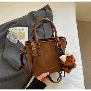 Brown patchwork bucket bag with teddy bear charm shown in an elegant lifestyle setting
