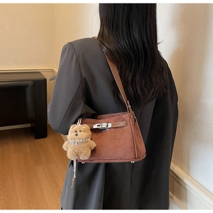 Detail of brown suede shoulder bag featuring a metal twist lock and a cute plush bear charm