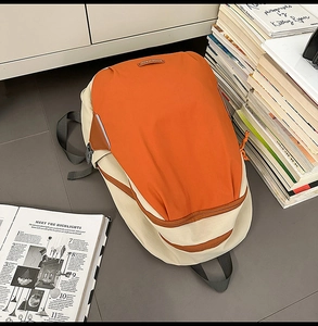 Detail of color-block backpack showing contrast orange zipper and adjustable straps