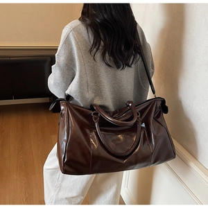 Détail d'un sac de voyage en cuir marron foncé porté à l'épaule par un mannequin