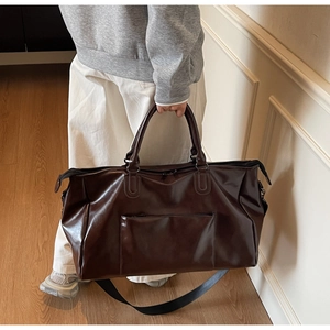 Détail du sac de voyage en cuir marron foncé avec bandoulière et poche zippée