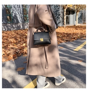 Close-up of black leather crossbody bag with gold buckle on model in beige coat