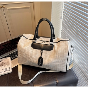 Close-up of white chevron woven travel bag with black leather handles and shoulder strap