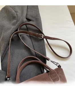 Detail of dark brown leather handbag with adjustable strap and silver buckle on a blazer