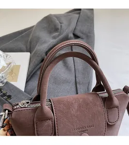 Detail view of the brown textured faux leather handbag with double handles and zipper