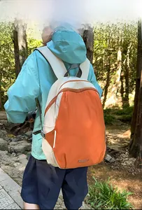 Outdoor model display of a lightweight contrast color backpack in orange and beige