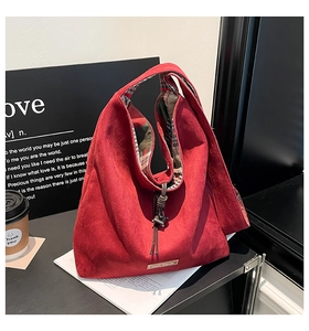 Detail of red faux suede tote bag with tartan lining and decorative tassel accents
