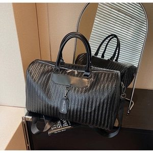 Detail of black woven texture travel bag with leather tag and adjustable shoulder strap