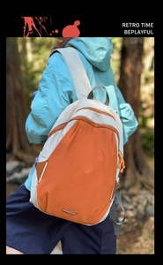 Detail of color-block backpack with orange paracord zippers in outdoor forest setting