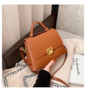 Detail of a brown leather handbag featuring a vintage gold metal clasp and top handle