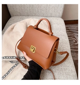 Detailed close-up of brown leather bag with gold buckle on a soft fabric background