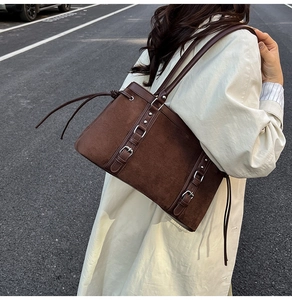 Detail of dark brown suede tote bag featuring decorative straps and long tassels