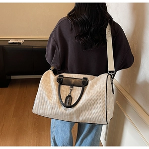 Detail view of woven cream travel bag featuring black leather handles and shoulder strap