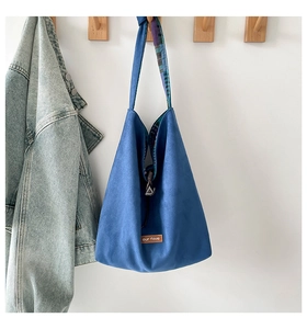 Detail of blue canvas tote bag showing the brown leather label and plaid fabric lining