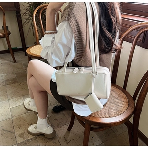 Detailed shot of cream rectangle box bag with dual zippers and mini hanging charm