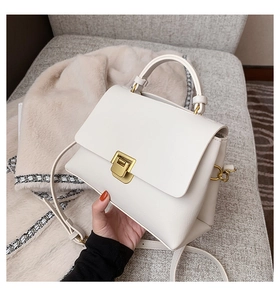 Detail of cream leather handbag featuring a golden buckle and elegant top handle