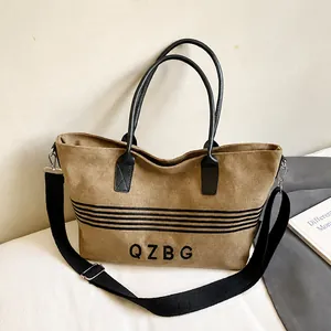 Brown striped canvas tote bag with black leather handles and adjustable crossbody strap