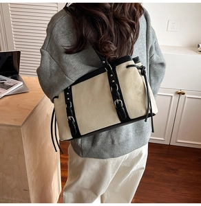 Detail view of large canvas tote bag with black leather trim and decorative buckles