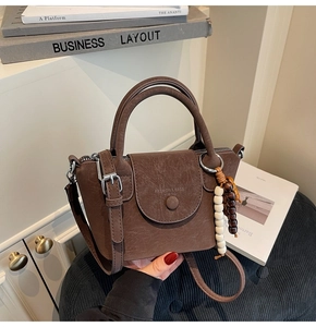 Detail of dark brown vintage crossbody bag with wooden bead charm on a minimalist desk