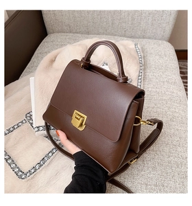 Detail of dark brown leather handbag with gold metal clasp on a gray sofa