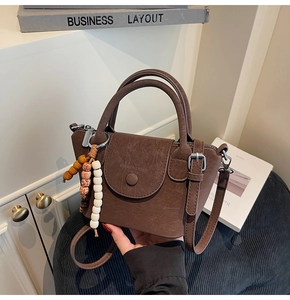 Detail shot of brown vintage textured handbag with beaded charm and embossed logo