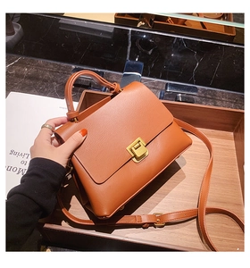 Close-up of caramel brown leather handbag with elegant gold metal lock on wooden tray