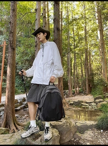 Outdoor hiking scene with a large black backpack and white hooded windbreaker in the woods