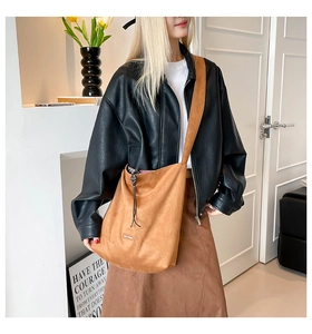 Detail of caramel suede bucket bag with wide shoulder strap and brand logo patch