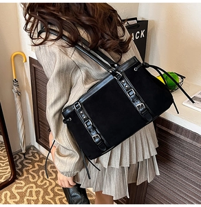 Detail view of large black suede tote bag with decorative buckle straps on model shoulder