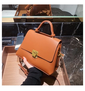 Close-up of orange-brown vintage square bag with gold buckle on marble background