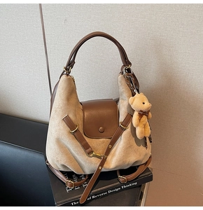 Close-up of khaki suede tote bag with brown leather handles and a plush bear charm