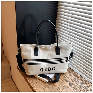 Detail of striped canvas tote bag with black leather handles on a wooden table